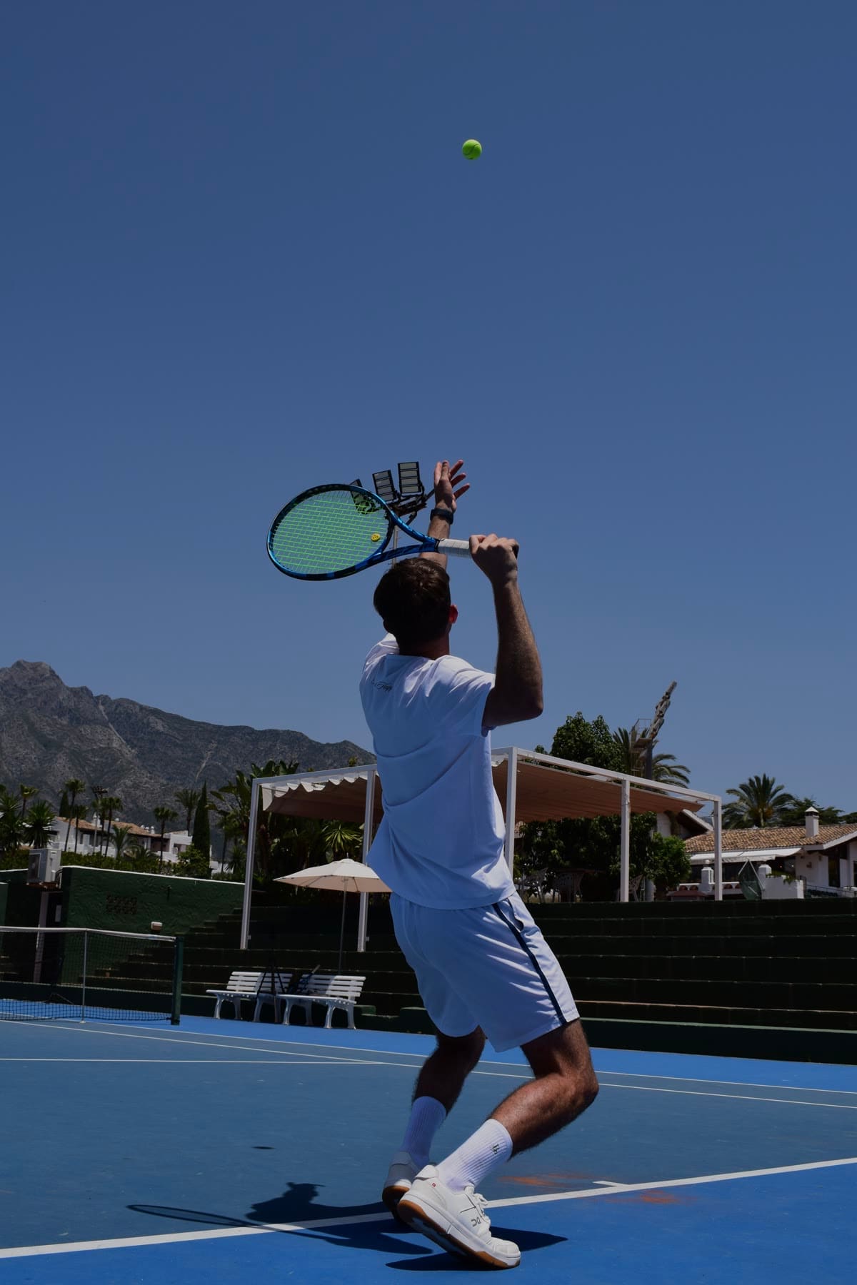 Saque de tenis en pista azul con montañas al fondo